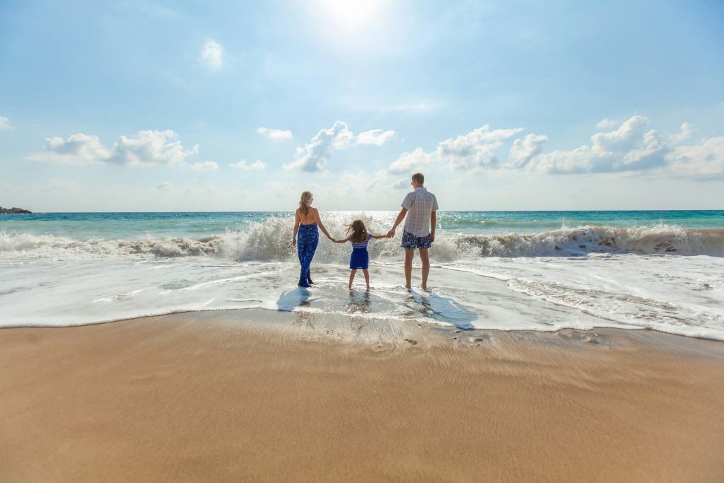 A family standing hand in hand on the beach with the waves crashing in front of them