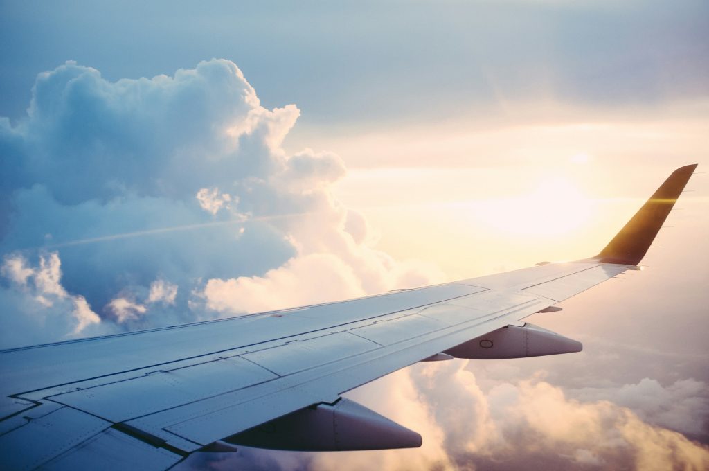A photo of a plane's wing in flight, with clouds and the sun in the background